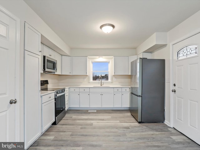 kitchen with white cabinets, stainless steel appliances, light hardwood / wood-style flooring, and sink