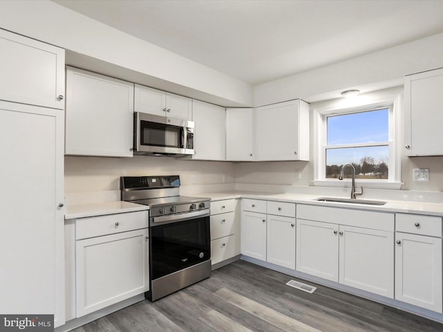 kitchen with appliances with stainless steel finishes, hardwood / wood-style flooring, white cabinetry, and sink