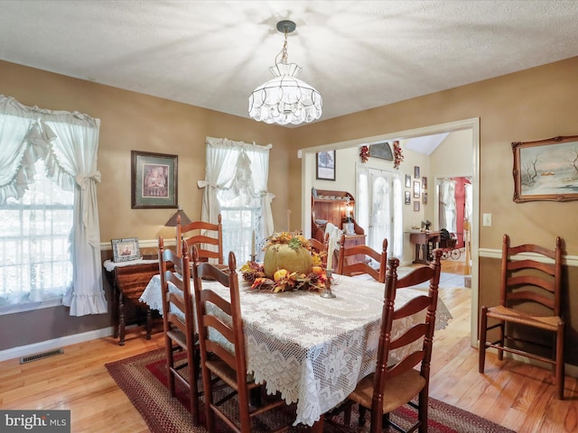 dining space with light wood-type flooring, a notable chandelier, and a textured ceiling