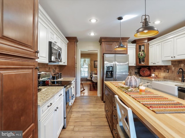 kitchen with stainless steel appliances, white cabinetry, light wood-type flooring, wood counters, and hanging light fixtures