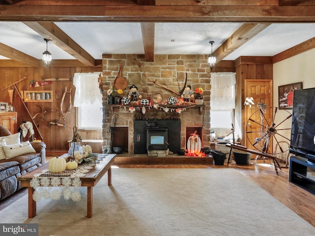 living room with a stone fireplace, beamed ceiling, wooden walls, and hardwood / wood-style flooring