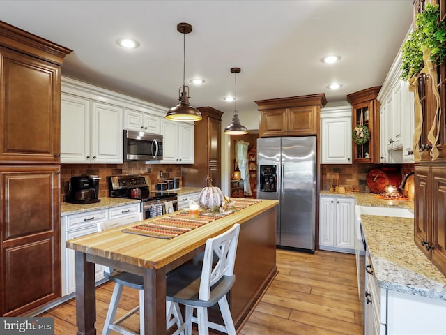 kitchen featuring stainless steel appliances, light hardwood / wood-style floors, hanging light fixtures, sink, and backsplash