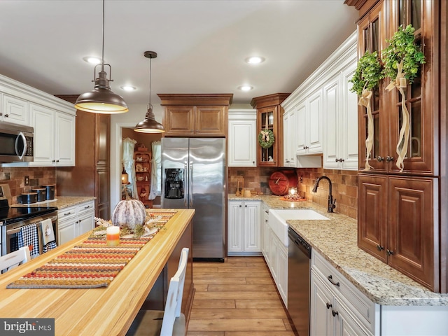 kitchen with stainless steel appliances, white cabinetry, sink, decorative light fixtures, and light hardwood / wood-style flooring