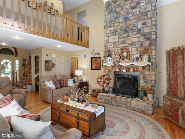 living room featuring a high ceiling, a stone fireplace, and light wood-type flooring