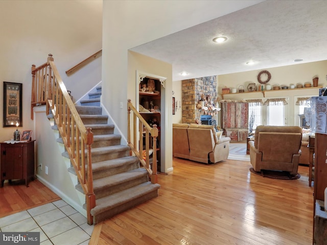 stairway featuring wood-type flooring, a textured ceiling, and a stone fireplace