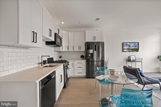 kitchen featuring stainless steel appliances, sink, light wood-type flooring, white cabinets, and tasteful backsplash