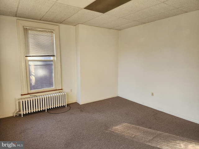 carpeted spare room featuring radiator and a drop ceiling