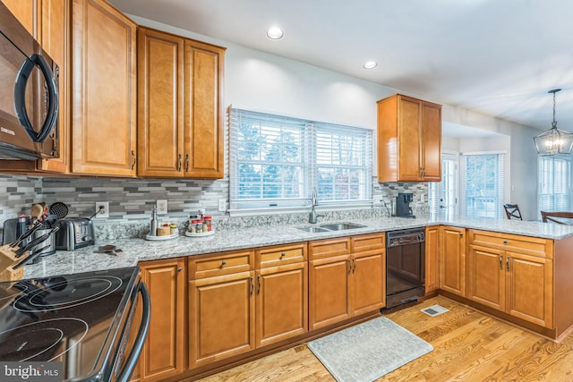 kitchen with a wealth of natural light, black appliances, decorative light fixtures, and light wood-type flooring