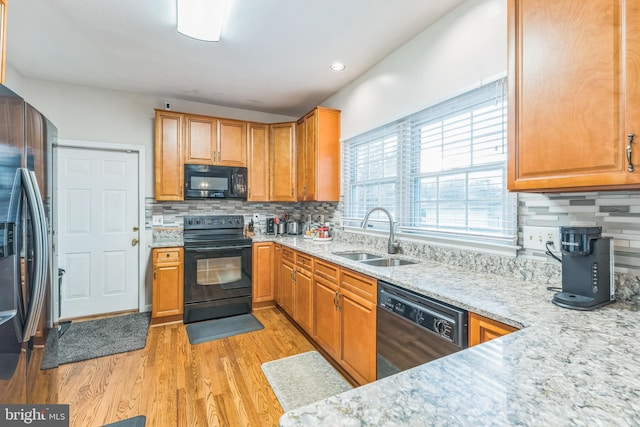 kitchen featuring backsplash, black appliances, sink, light hardwood / wood-style flooring, and light stone counters