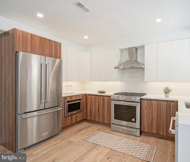 kitchen with light hardwood / wood-style floors, wall chimney exhaust hood, white cabinets, and stainless steel appliances