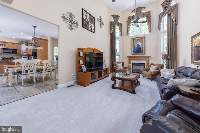 carpeted living room featuring a towering ceiling and ceiling fan with notable chandelier