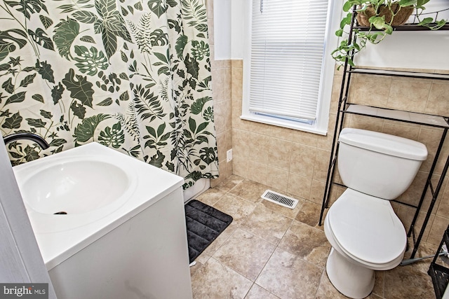 bathroom featuring vanity, tile walls, toilet, and walk in shower