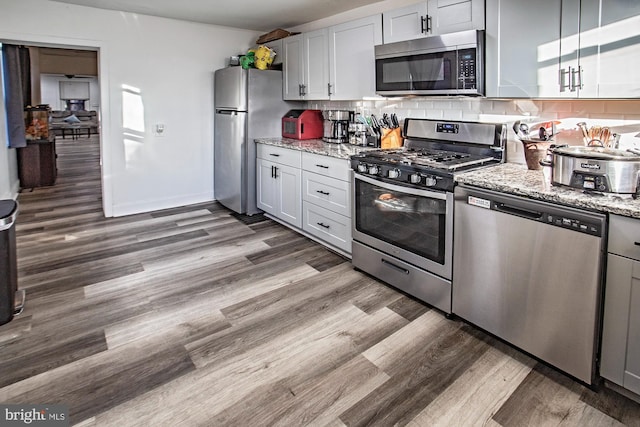 kitchen featuring light stone counters, stainless steel appliances, decorative backsplash, and wood-type flooring