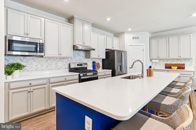 kitchen featuring a breakfast bar area, an island with sink, sink, light wood-type flooring, and appliances with stainless steel finishes