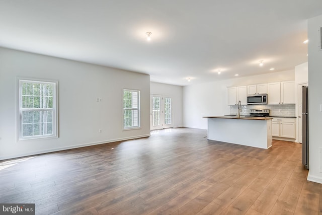 kitchen with appliances with stainless steel finishes, light wood-type flooring, white cabinetry, decorative backsplash, and a kitchen island with sink