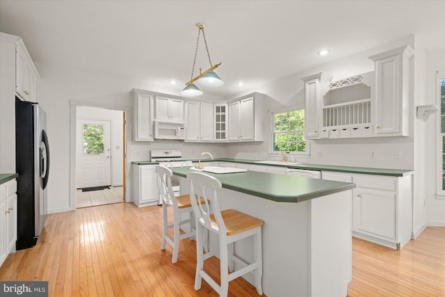 kitchen featuring a breakfast bar area, light hardwood / wood-style flooring, an island with sink, white cabinets, and white appliances