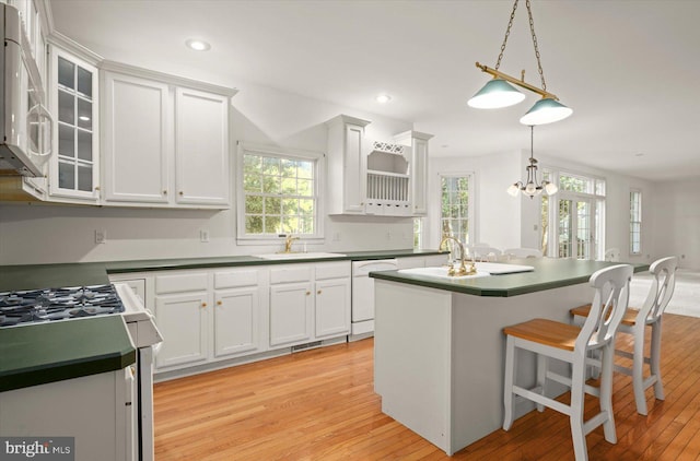 kitchen featuring white cabinets, a breakfast bar area, light hardwood / wood-style flooring, pendant lighting, and white appliances