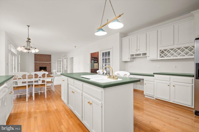 kitchen featuring light wood-type flooring, a brick fireplace, white cabinetry, pendant lighting, and a center island with sink