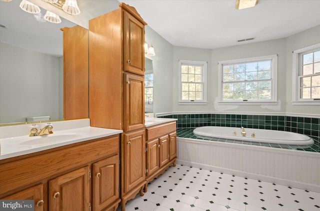 bathroom with vanity, toilet, a relaxing tiled tub, and a wealth of natural light