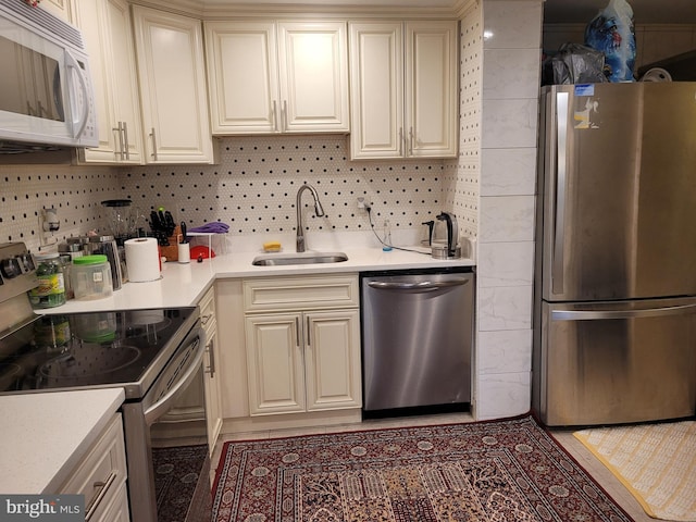 kitchen with backsplash, appliances with stainless steel finishes, sink, and cream cabinets