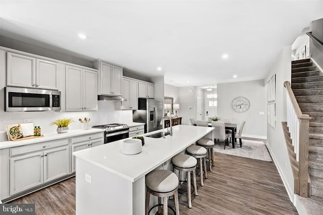 kitchen with a breakfast bar area, a center island with sink, sink, appliances with stainless steel finishes, and dark hardwood / wood-style flooring