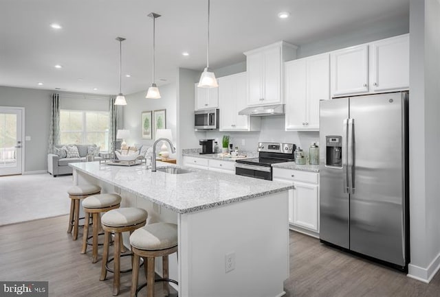 kitchen with an island with sink, sink, white cabinets, pendant lighting, and appliances with stainless steel finishes