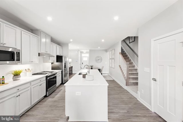 kitchen featuring sink, white cabinetry, light hardwood / wood-style floors, stainless steel appliances, and a center island with sink