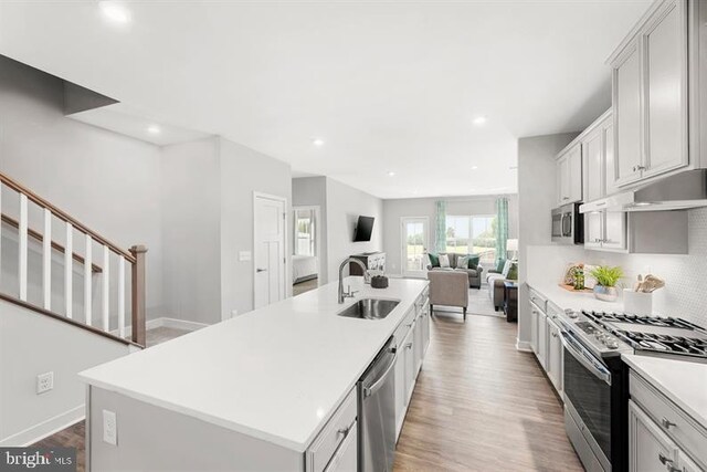 kitchen featuring appliances with stainless steel finishes, white cabinetry, a kitchen island with sink, light wood-type flooring, and sink