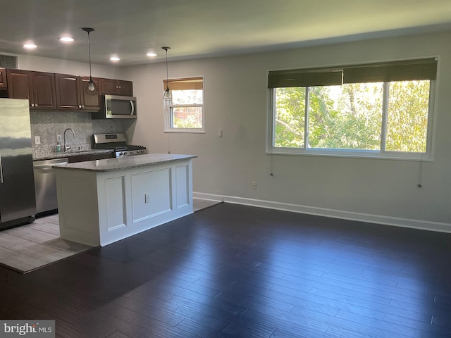 kitchen featuring a kitchen island, hardwood / wood-style flooring, hanging light fixtures, stainless steel appliances, and backsplash