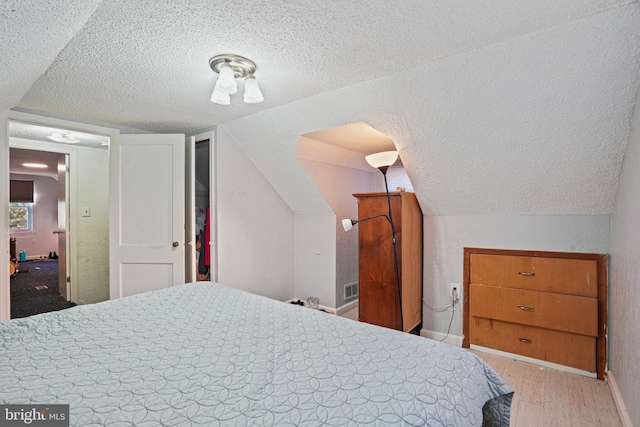 bedroom featuring light hardwood / wood-style flooring, a textured ceiling, and vaulted ceiling