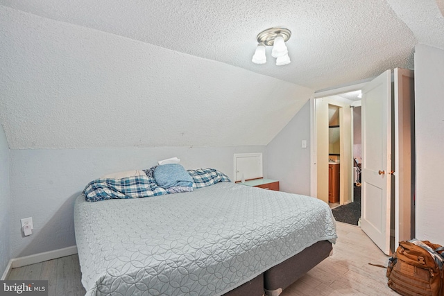 bedroom with lofted ceiling, a textured ceiling, and light hardwood / wood-style floors