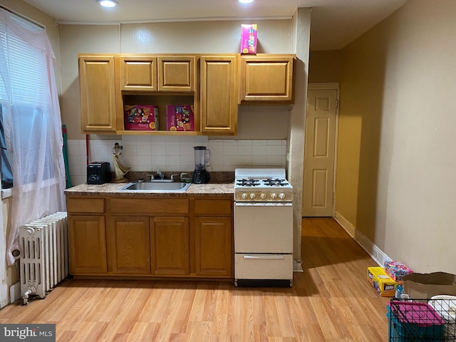 kitchen featuring backsplash, radiator, sink, white gas range oven, and light hardwood / wood-style floors