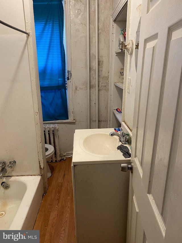 bathroom with radiator, a washtub, hardwood / wood-style floors, toilet, and vanity