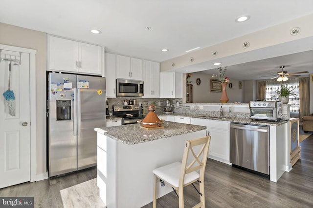 kitchen with sink, a kitchen island, white cabinetry, stainless steel appliances, and dark wood-type flooring