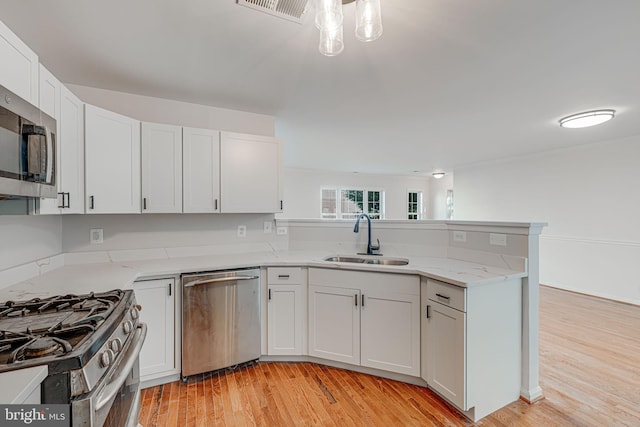 kitchen with kitchen peninsula, white cabinetry, light wood-type flooring, sink, and stainless steel appliances