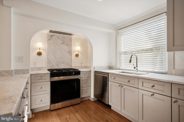 kitchen with light stone counters, sink, light wood-type flooring, and stainless steel appliances