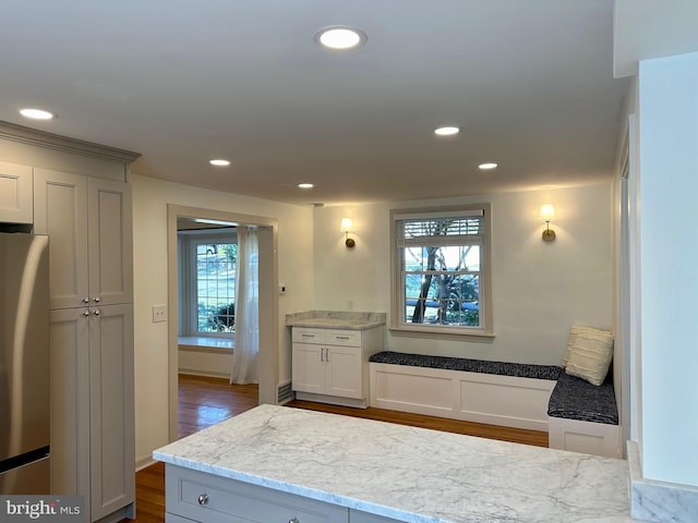 kitchen featuring stainless steel fridge, light stone counters, and dark wood-type flooring