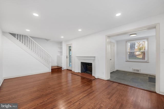 unfurnished living room with wood-type flooring and a brick fireplace