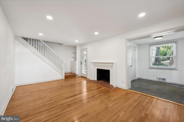 unfurnished living room with hardwood / wood-style floors, built in shelves, and a fireplace