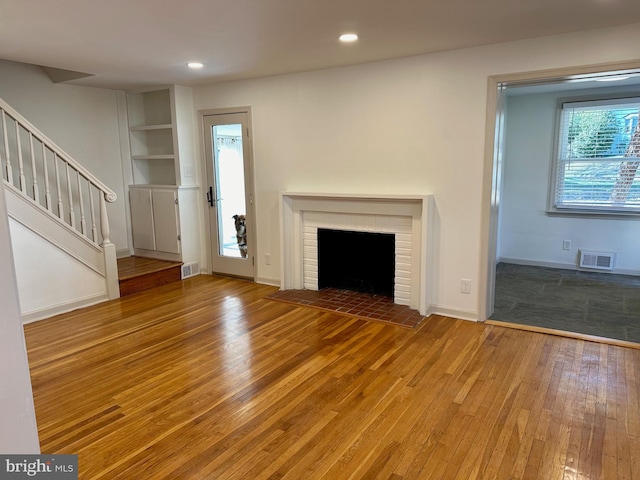 unfurnished living room with a fireplace, wood-type flooring, and built in features