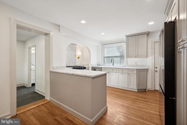 kitchen featuring light stone counters, light wood-type flooring, kitchen peninsula, and stainless steel appliances