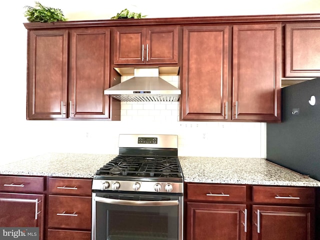 kitchen featuring stainless steel range with gas stovetop, decorative backsplash, light stone countertops, and wall chimney range hood