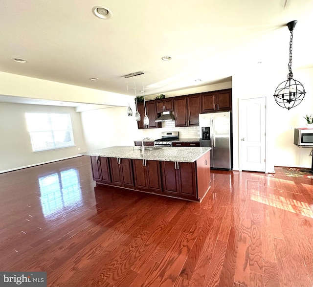 kitchen with appliances with stainless steel finishes, dark hardwood / wood-style flooring, pendant lighting, and a center island with sink