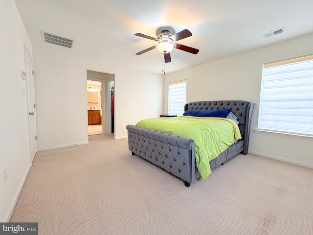 bedroom with multiple windows, ceiling fan, ensuite bathroom, and light colored carpet