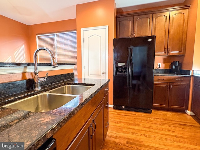 kitchen with dark stone countertops, black fridge with ice dispenser, light hardwood / wood-style floors, and sink