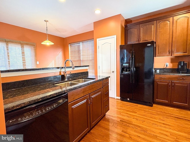 kitchen with dark stone counters, sink, black appliances, light hardwood / wood-style floors, and hanging light fixtures