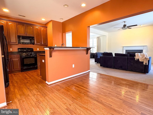 kitchen featuring hardwood / wood-style flooring, ceiling fan, a breakfast bar area, and black appliances