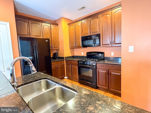 kitchen with light wood-type flooring, sink, dark stone countertops, and black appliances