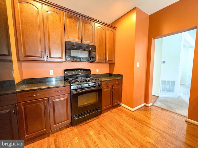 kitchen with light hardwood / wood-style flooring, dark stone counters, and black appliances