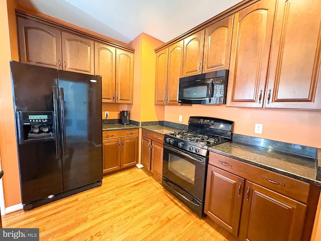 kitchen with dark stone countertops, black appliances, lofted ceiling, and light hardwood / wood-style floors